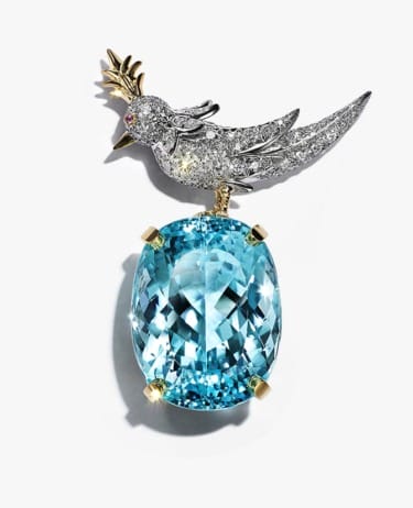 Exquisite bird-shaped brooch with diamonds and a large blue gemstone centerpiece on a white background.