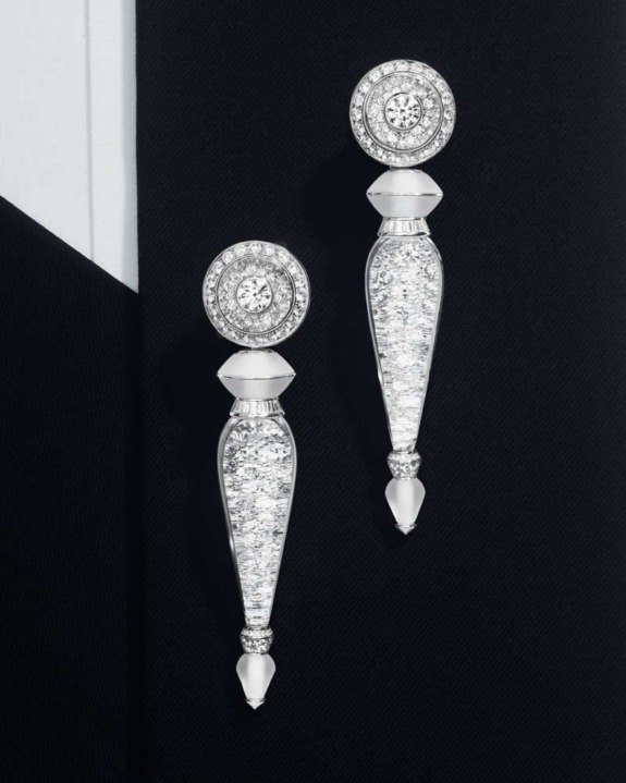 Elegant diamond and silver drop earrings with intricate detailing displayed on a dark textured background.