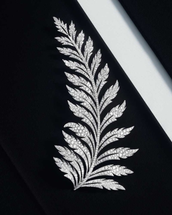 Diamond-studded brooch with intricate leaf design on a black fabric background.