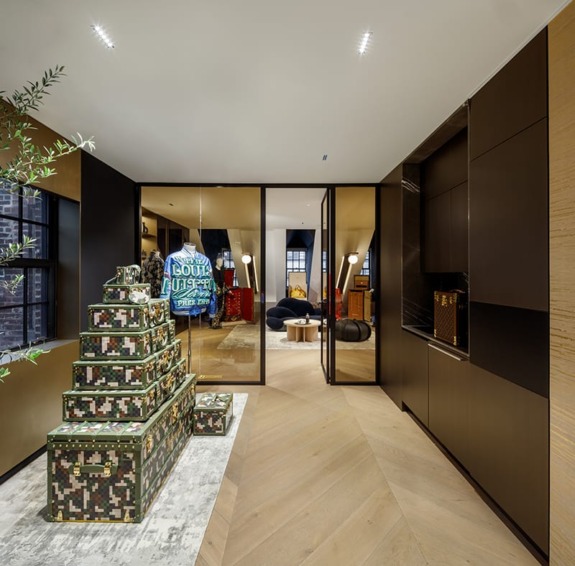Luxurious modern hallway with stacked designer trunks, glass doors, and stylish seating area in the background.