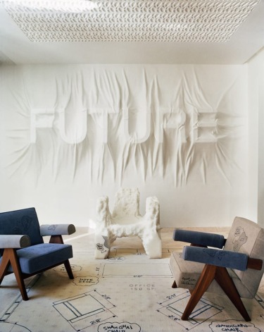 Modern interior with textured wall art spelling "FUTURE," unique white chair, and two wooden armchairs on patterned floor.