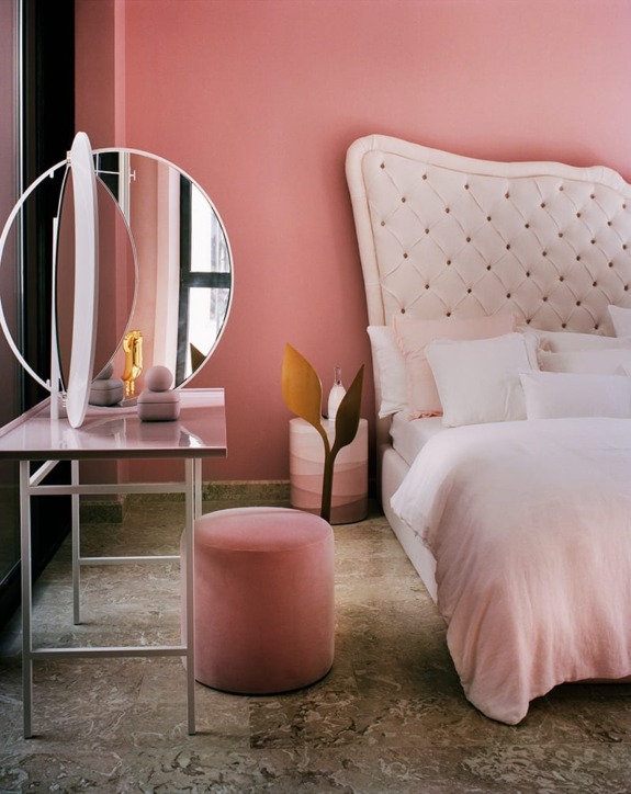 Elegant bedroom with a pink theme, featuring a tufted headboard, round vanity mirror, and plush pink stool.