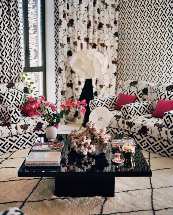 Modern living room with patterned curtains and furniture, black coffee table, floral arrangements, and decorative elements.
