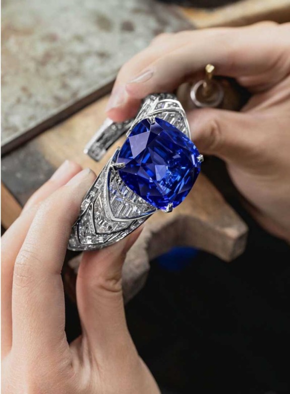 Craftsman holding an ornate silver ring with a large blue gemstone and intricate detailing.