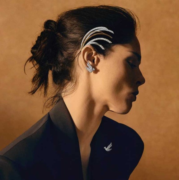 Woman wearing black outfit and elegant silver accessories with a minimalist hairstyle, set against a warm brown background.