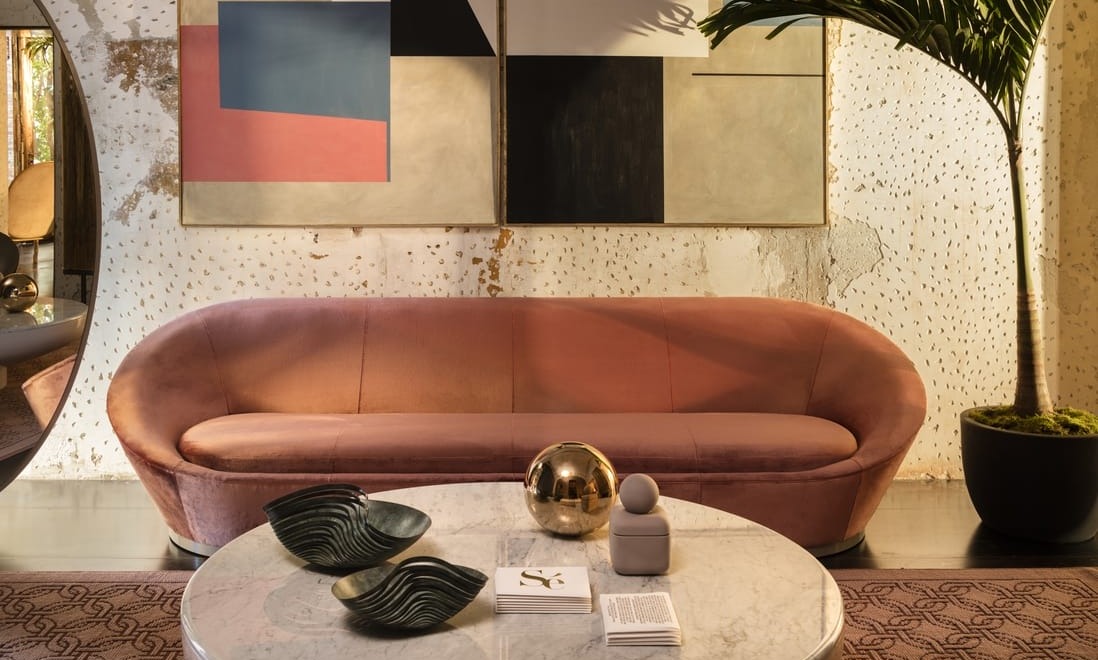 Stylish living room with a pink sofa, abstract art, round marble coffee table, and a tall potted plant.