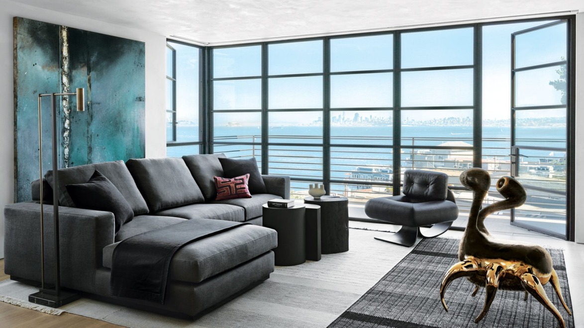 Modern living room with dark furniture, large windows overlooking a cityscape, and a unique artistic sculpture on the floor.