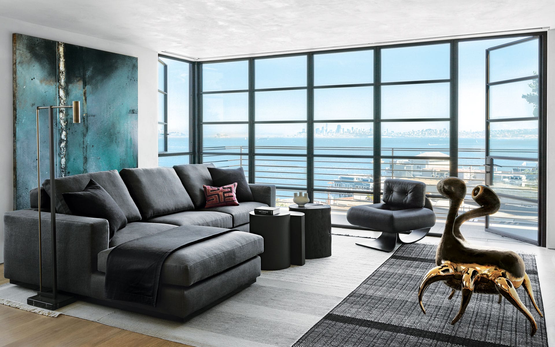 Modern living room with dark furniture, large windows overlooking a cityscape, and a unique artistic sculpture on the floor.
