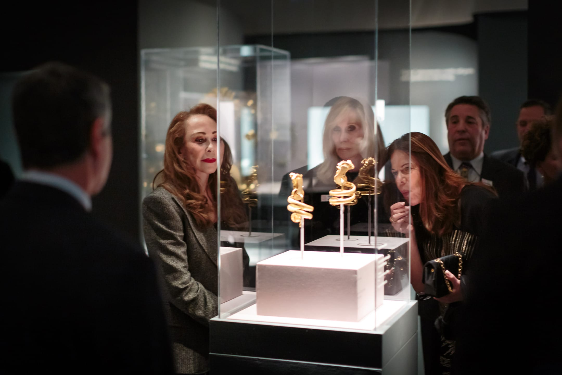 People observing gold artifacts displayed in a museum exhibition.