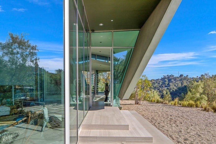 Modern glass building with angled roof, surrounded by trees and clear sky, reflecting the natural landscape in windows.