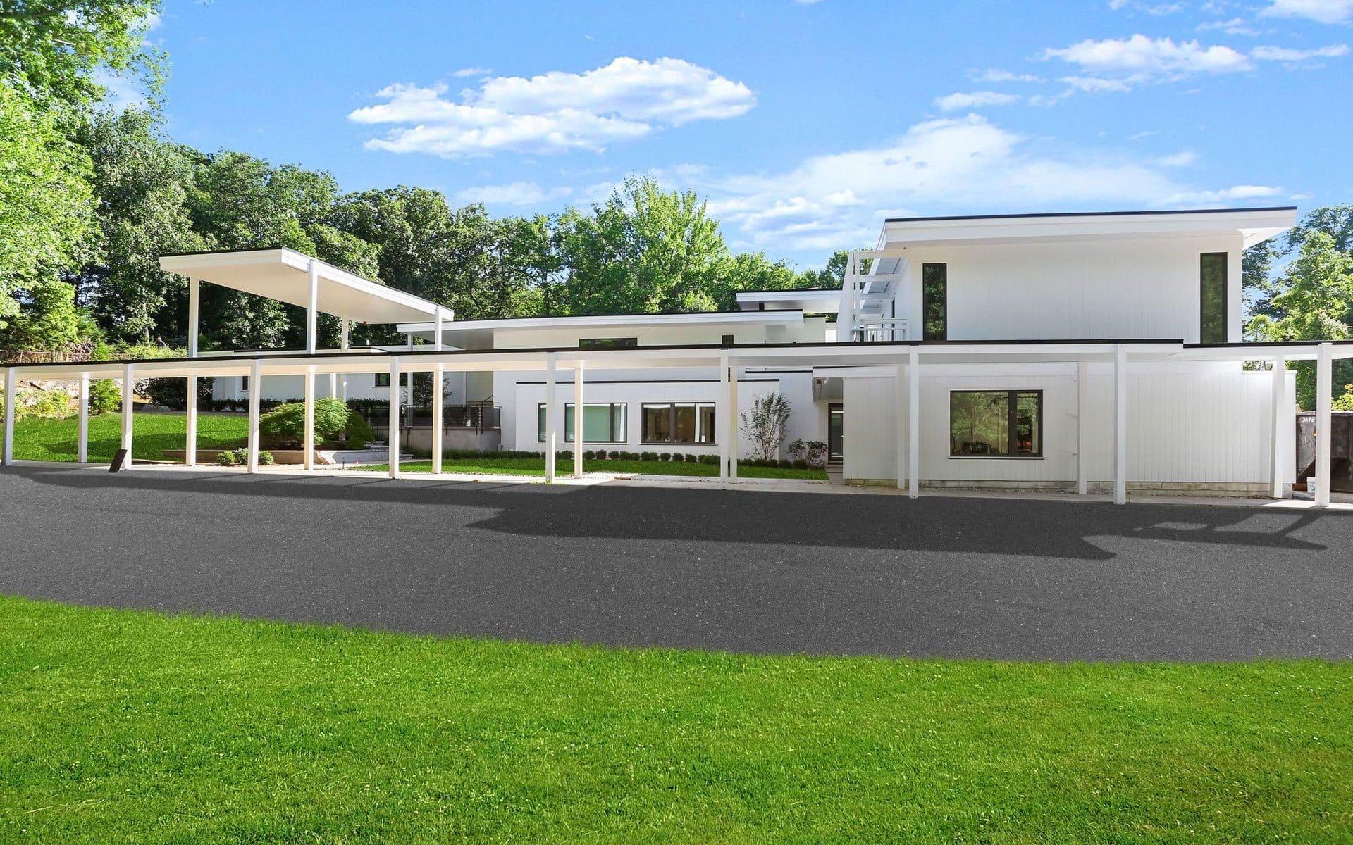 Modern white architectural building with large windows and a flat roof surrounded by trees and a well-maintained lawn.