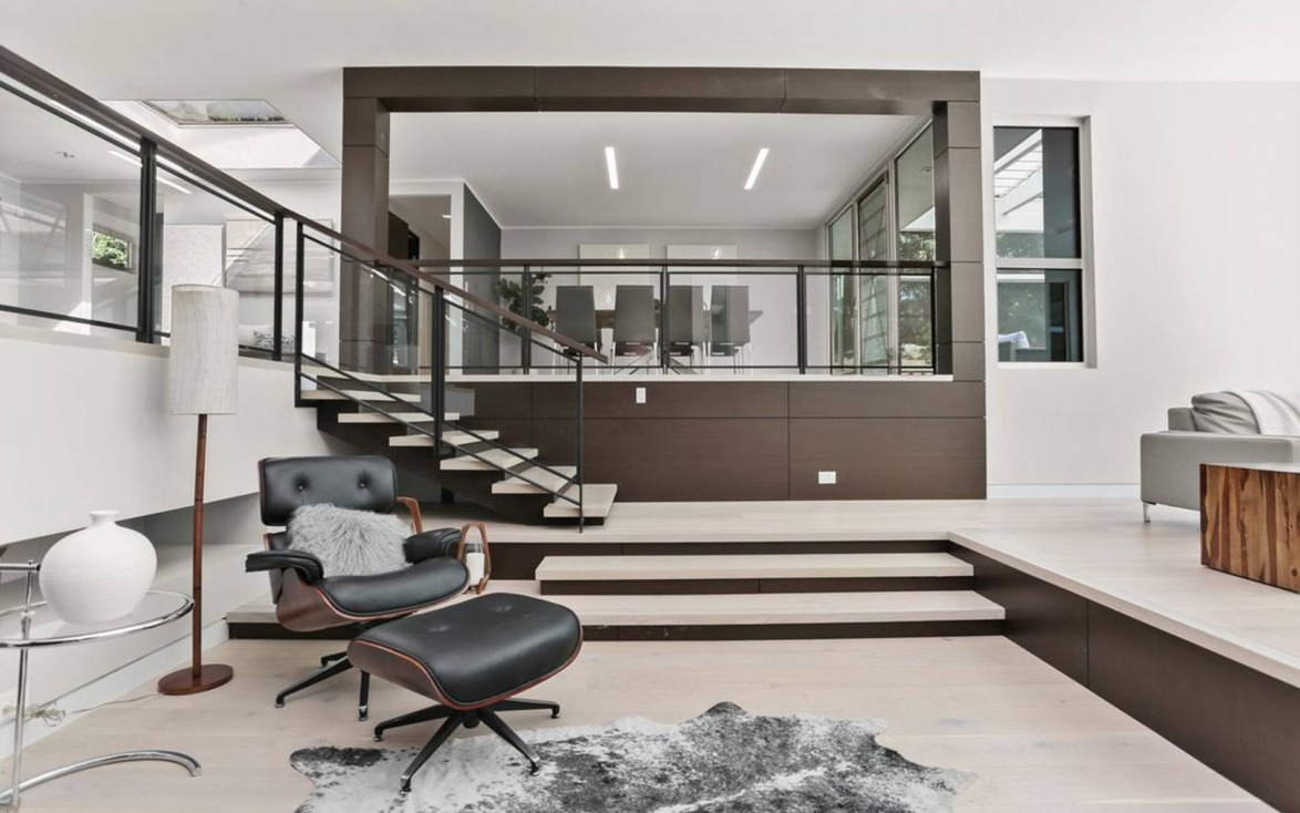 Modern interior with a stylish lounge chair and stairs leading to a glass-walled office space.