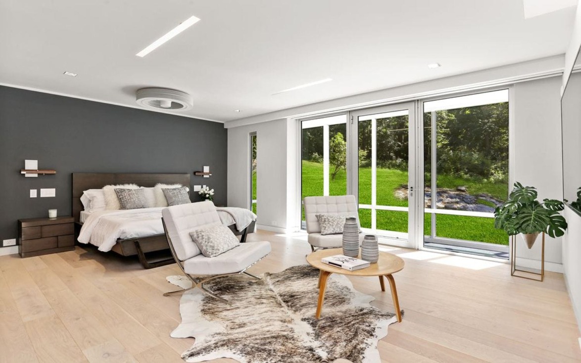 Modern bedroom with large windows, double bed, two chairs, a round table, and a faux fur rug on light wood floors.