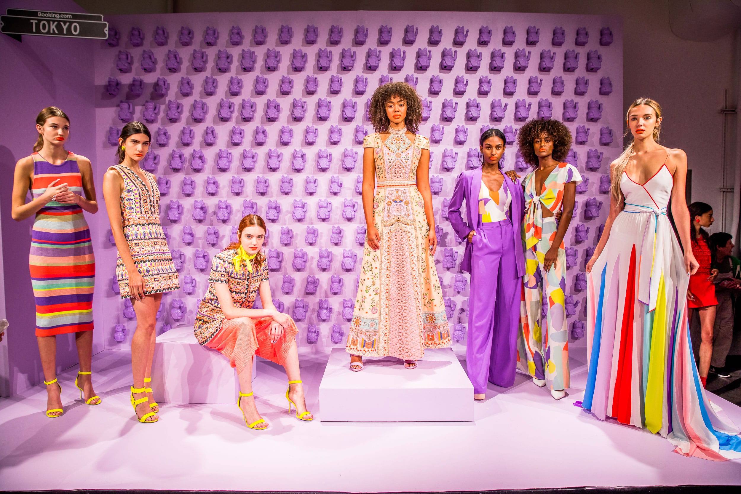 Fashion models showcasing vibrant, patterned outfits on a colorful runway background with artistic wall designs.