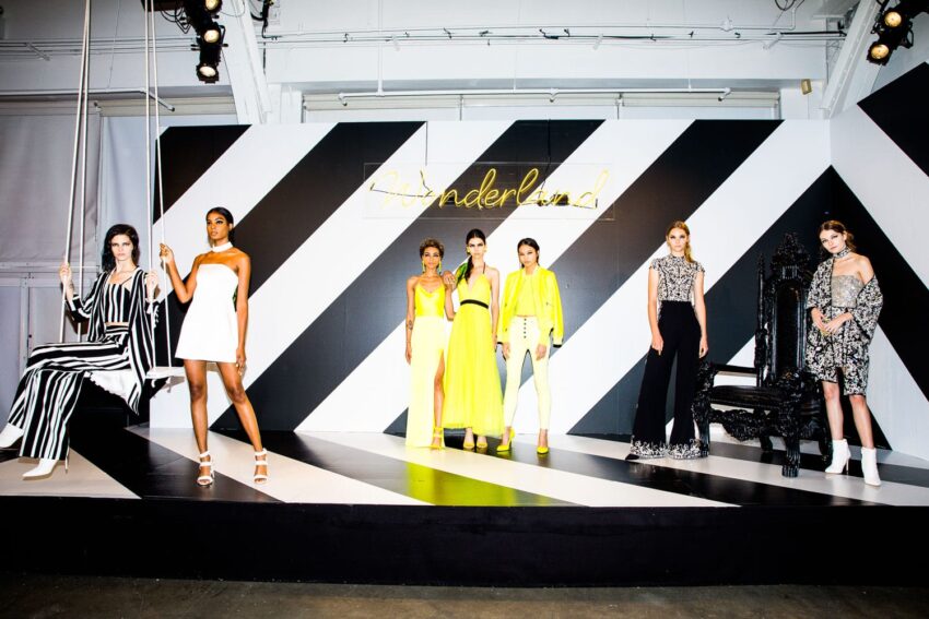 Fashion models on stage wearing colorful and stylish outfits against a geometric black and white backdrop.