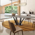 Modern dining room with oval table, chairs, and a large window overlooking a garden.