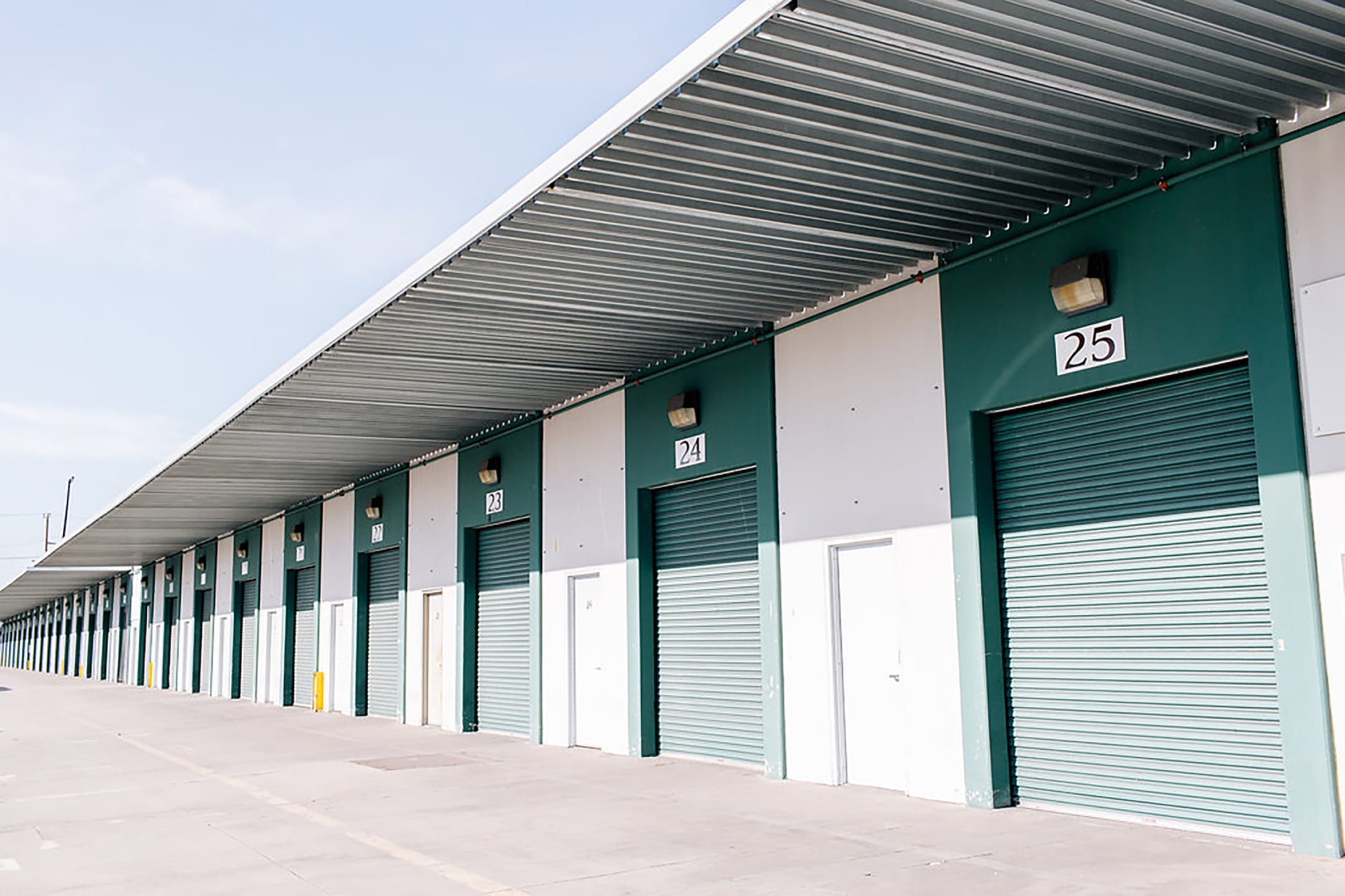 Row of green and white industrial storage units with numbered rolling doors in an outdoor facility.