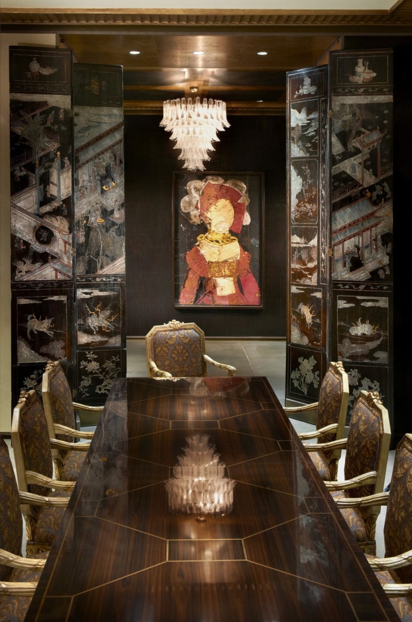 Elegant dining room with a dark wooden table, ornate chairs, a chandelier, and a decorative wall panel featuring artwork.