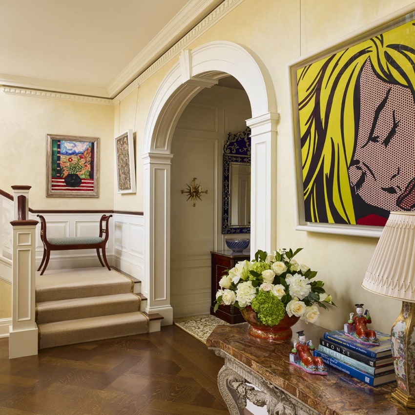 Elegant hallway with colorful pop art, archway, and floral arrangement on a marble console table next to a staircase.