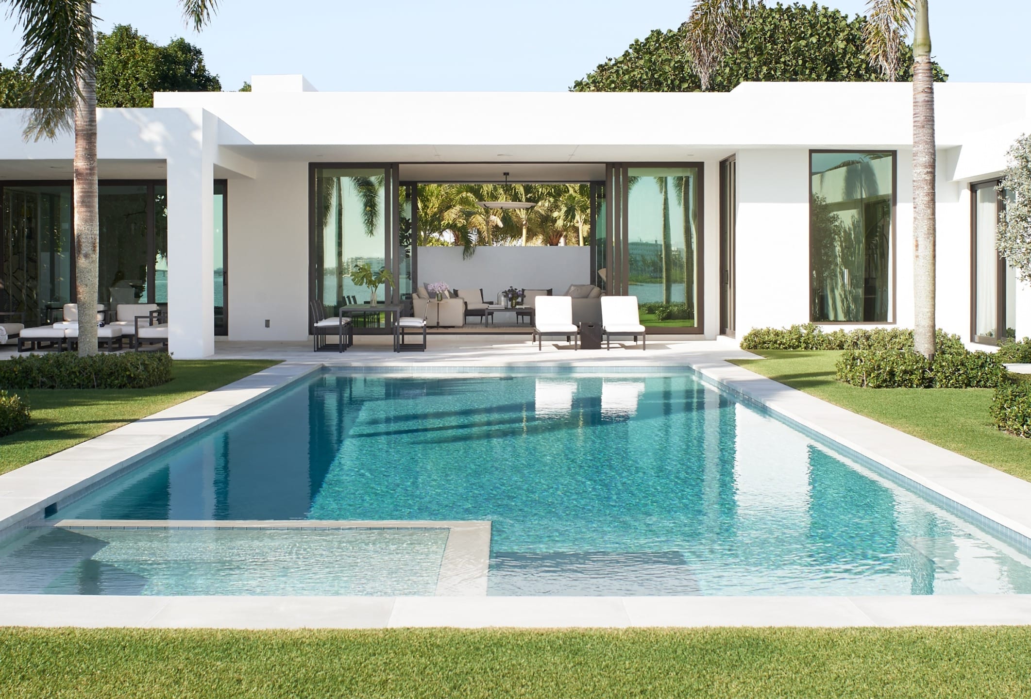 Modern house with large glass doors and a swimming pool in the foreground, surrounded by well-maintained green lawn.