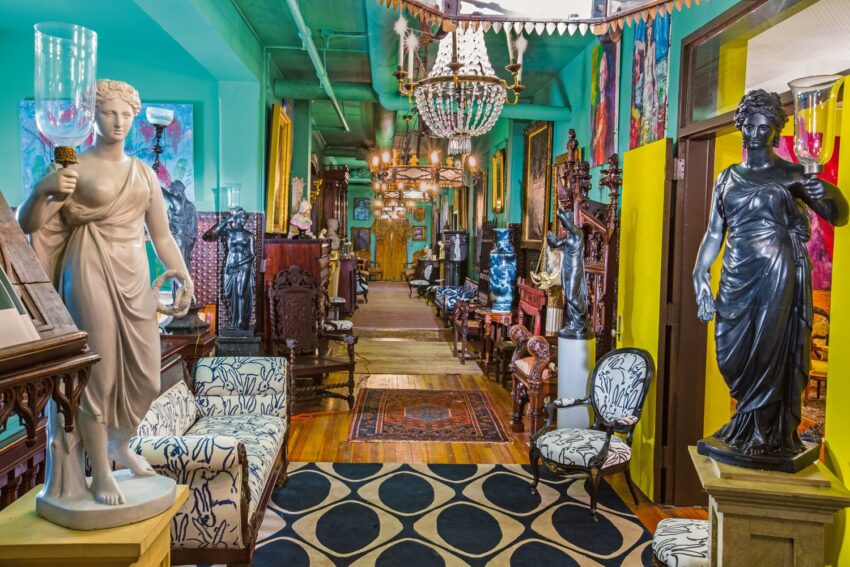 Eclectic antique shop interior with statues, vintage furniture, chandeliers, and colorful decor, creating a vibrant atmosphere.