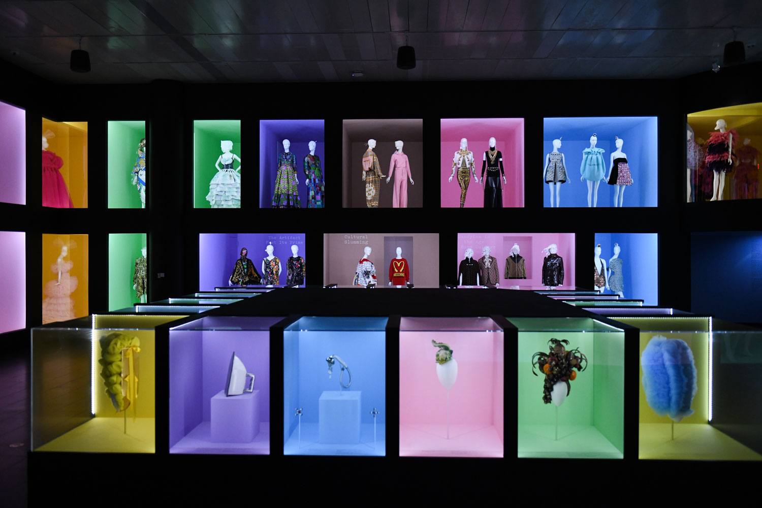 Colorful displays of fashion mannequins and artistic items in a modern exhibit with vibrant lighting and diverse designs.