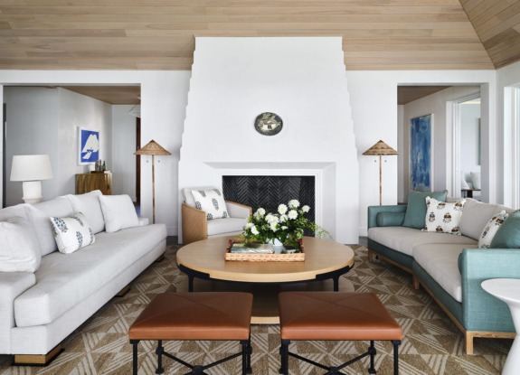 Modern living room with white sofas, wooden coffee table, fireplace, and decorative plants in a bright, stylish space.