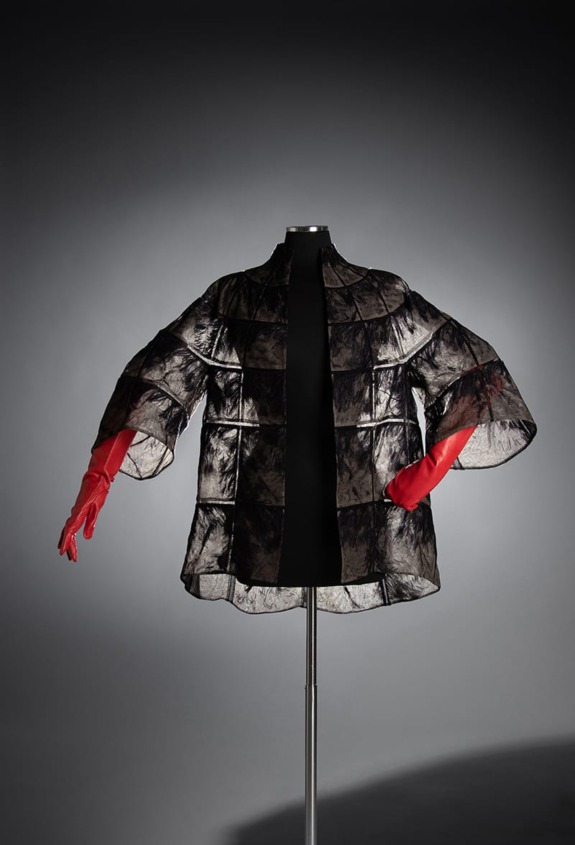 Black and transparent textured coat with red gloves displayed on a mannequin against a dark background.