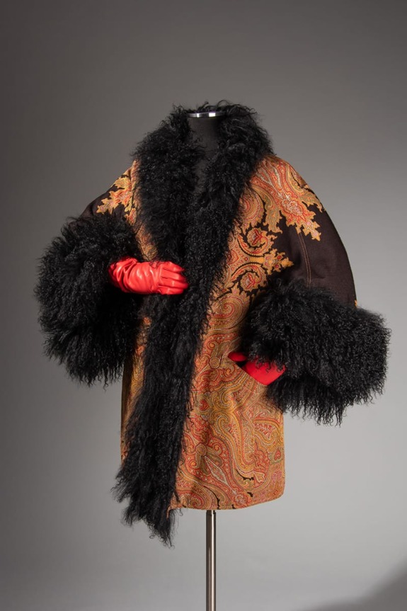 Vintage paisley coat with black fur trim and red gloves on mannequin against a gray background