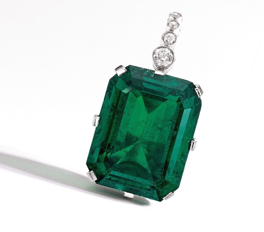 Emerald-cut green gemstone pendant with diamond accents on a white background.