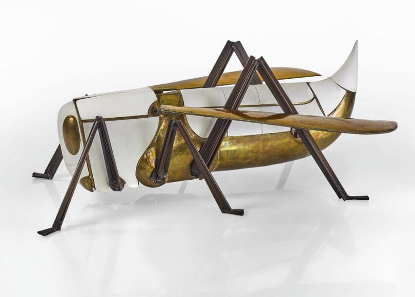 Sculpture of a grasshopper with a body resembling an airplane, featuring brass and white elements on display.