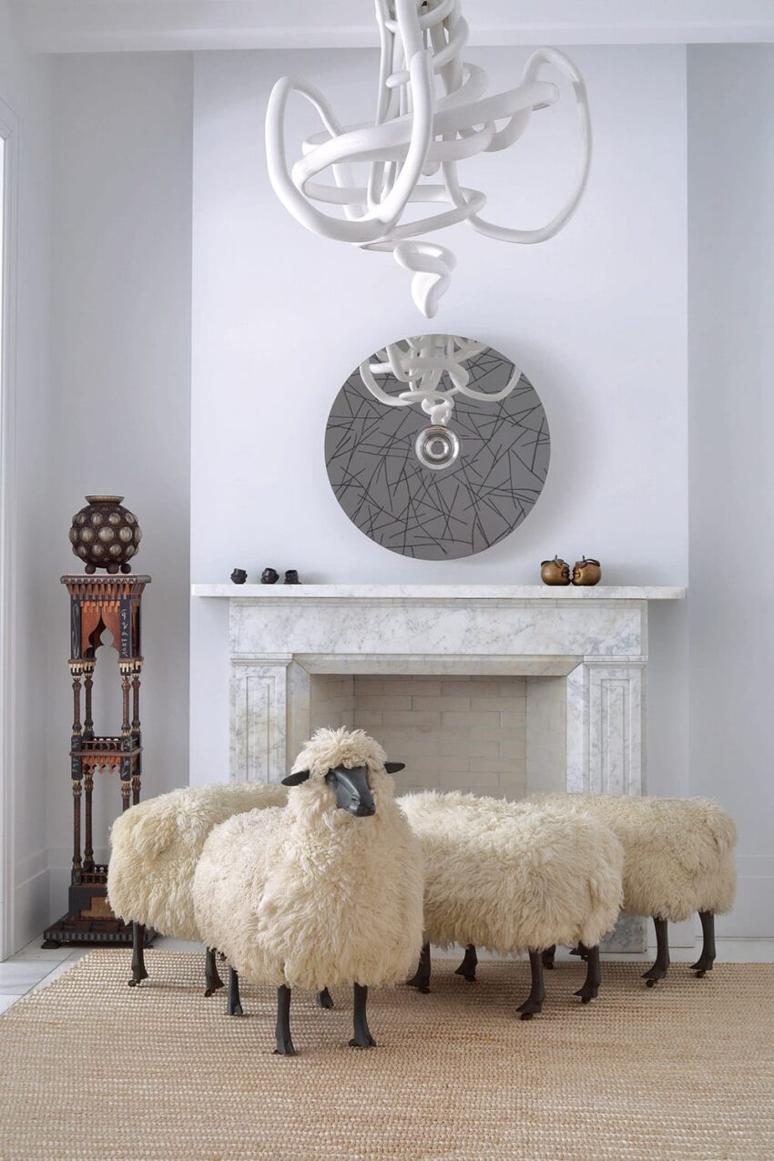 Stylish room with fluffy sheep sculptures, marble fireplace, a mirror, unique chandelier, and decorative stand.