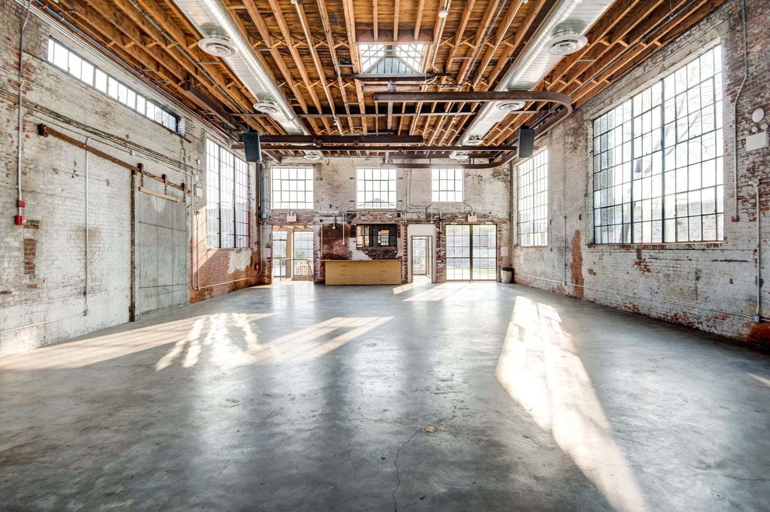 Spacious industrial loft with exposed brick walls, large windows, and high wooden ceilings.