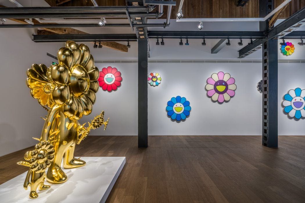 Contemporary art gallery with colorful flower-themed artworks on walls and a large golden flower sculpture in the foreground