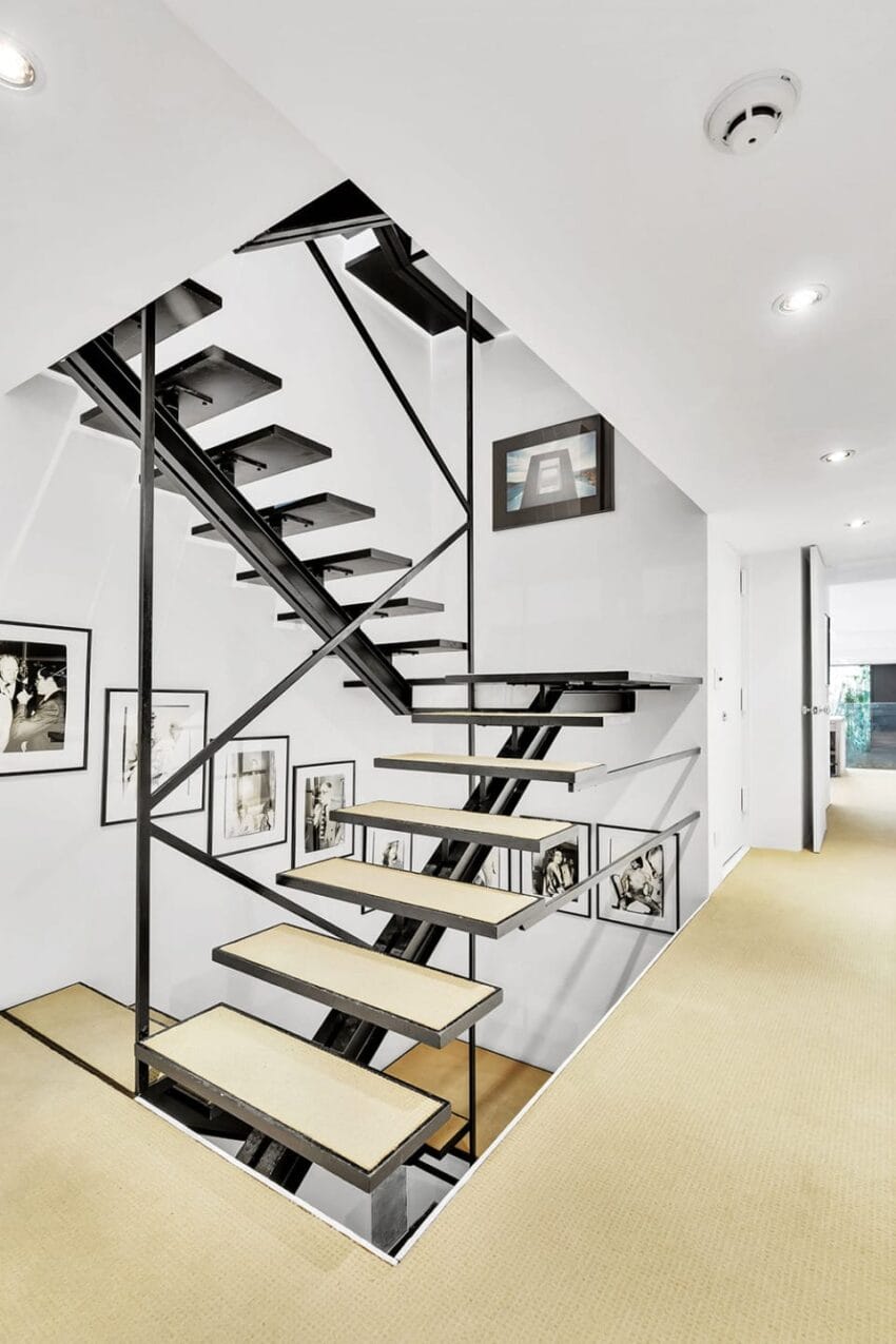 Modern interior staircase with sleek black metal railings, carpeted steps, and surrounding art on white walls.