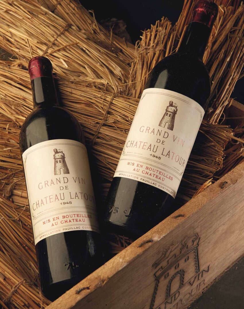 Two bottles of 1945 Grand Vin de Chateau Latour wine resting on straw in a wooden crate.