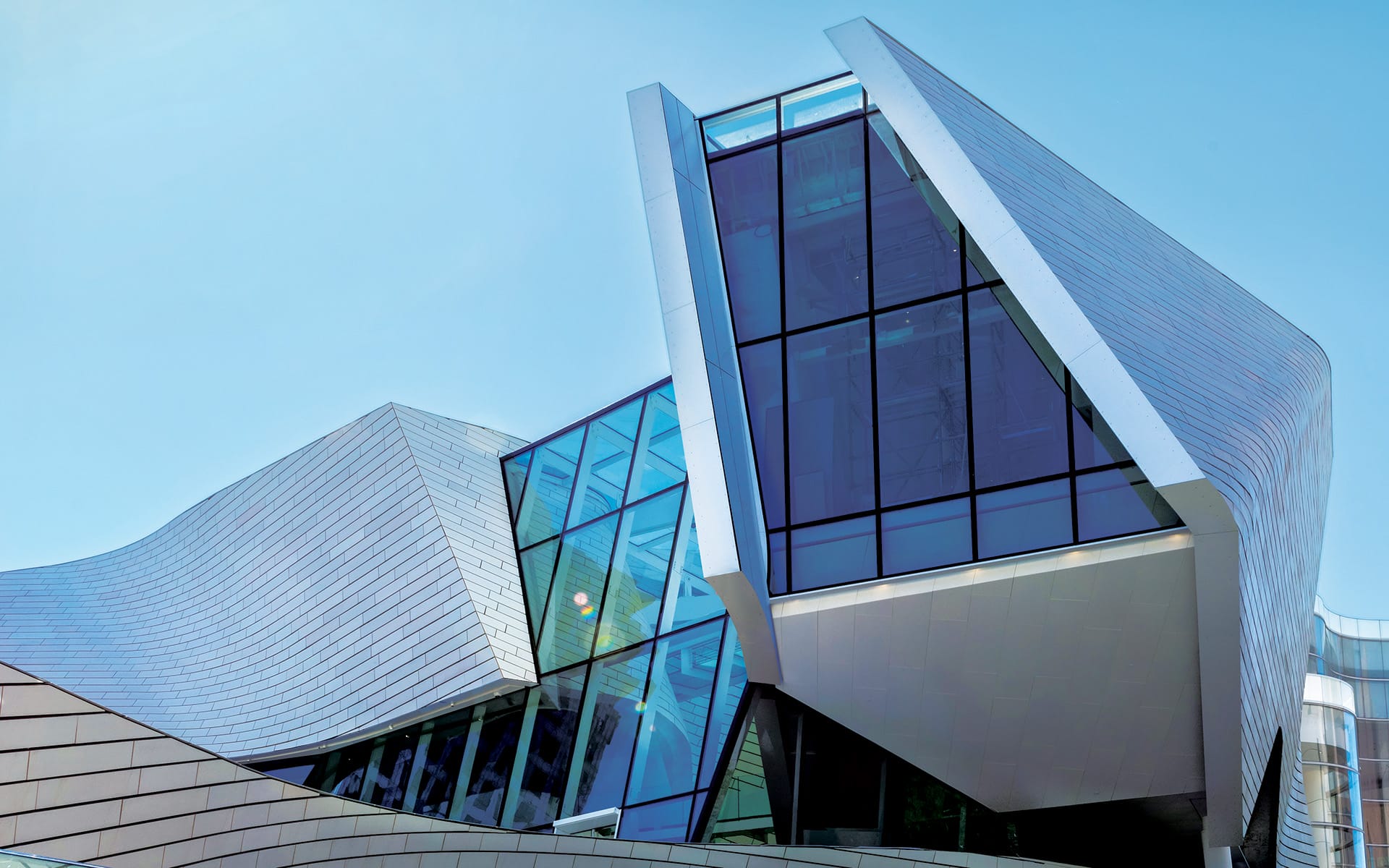 Modern architectural building with glass and metal facade under clear blue sky.
