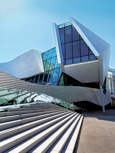 Modern architectural building with angular design, large glass windows, and a staircase under a clear blue sky.