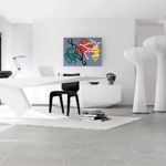 Modern minimalist office with geometric white desk, black chair, abstract wall art, and large window views of greenery.
