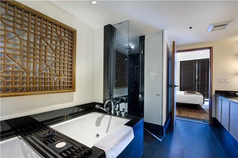 Modern bathroom with a large white bathtub, decorative wooden wall panel, glass shower, and dark tiled floor.