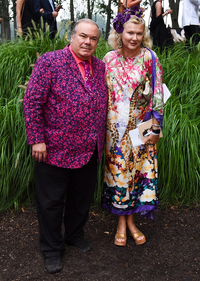 Couple in vibrant, colorful outfits standing outdoors with greenery in the background.