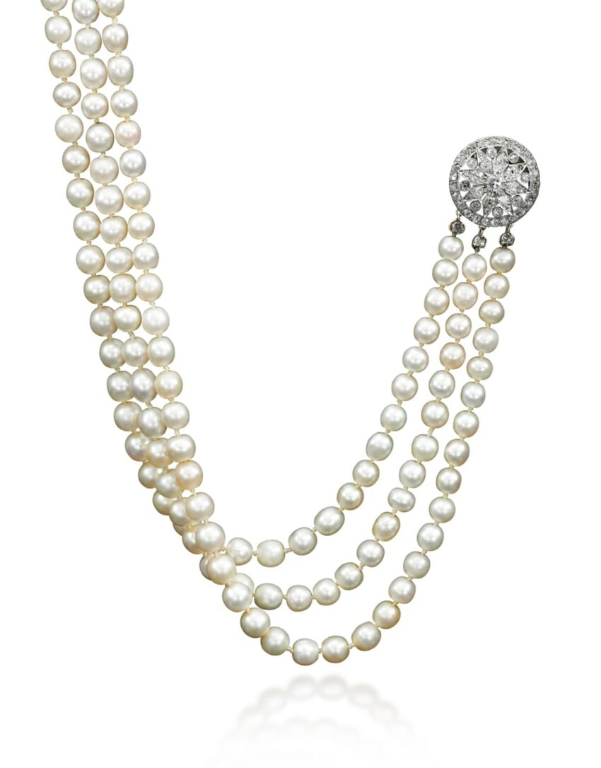 Triple-strand pearl necklace with a diamond-studded circular clasp displayed against a white background.