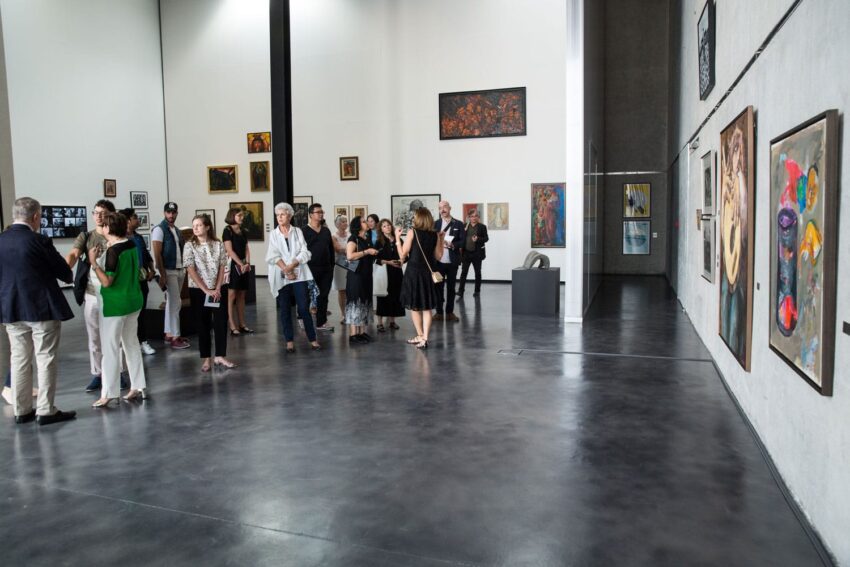 Group of people admiring artwork in a modern art gallery with paintings displayed on white and grey walls.