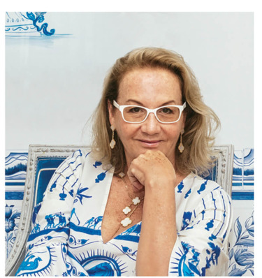 Woman with glasses in blue and white dress sitting and smiling.