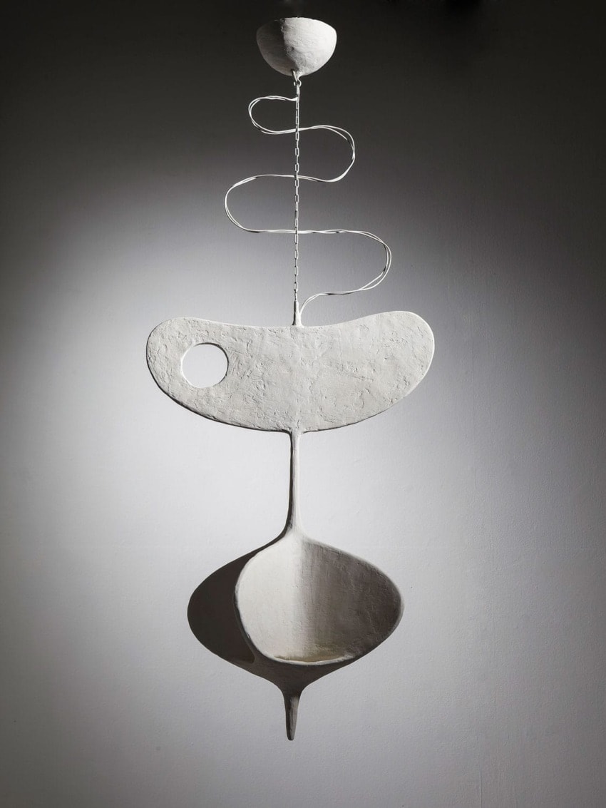Abstract white sculpture against a gray background with flowing and curved shapes, suspended by a thin wire.