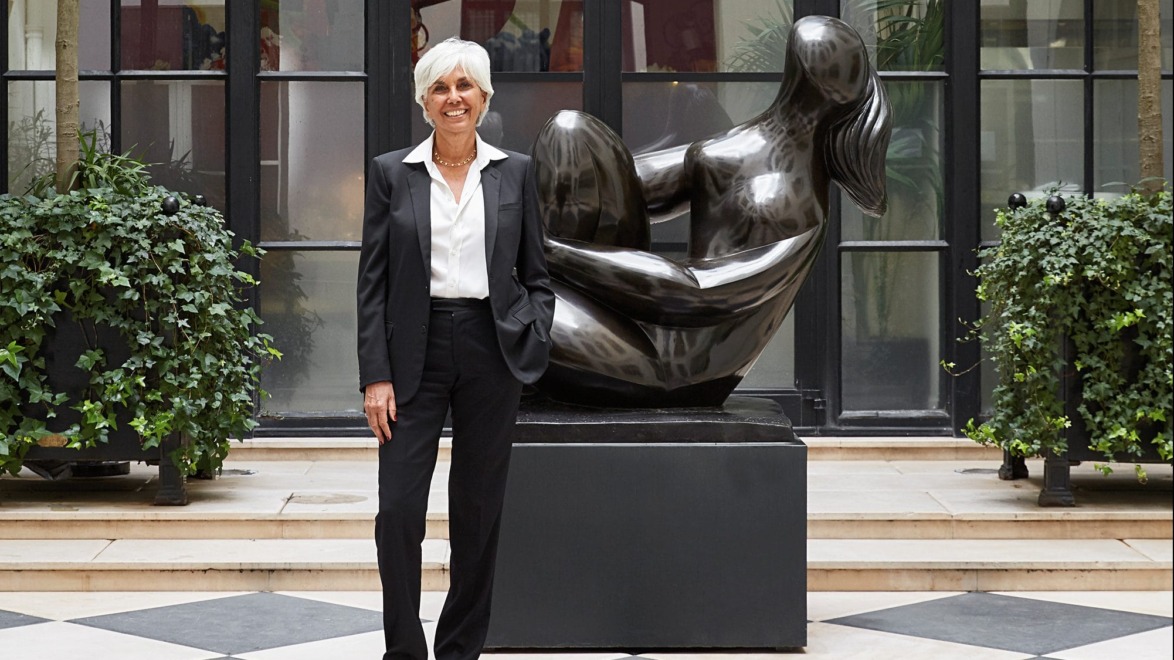 Person in a suit standing in a stylish atrium with a modern sculpture in the background and plants on either side.