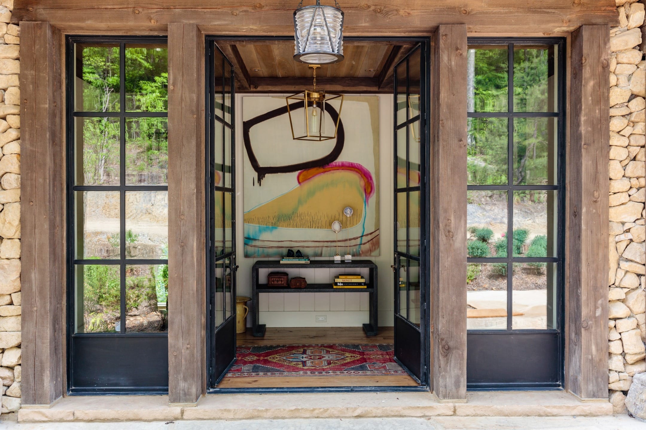 Rustic entrance with stone walls, glass doors, colorful abstract art, and a decorative light fixture.