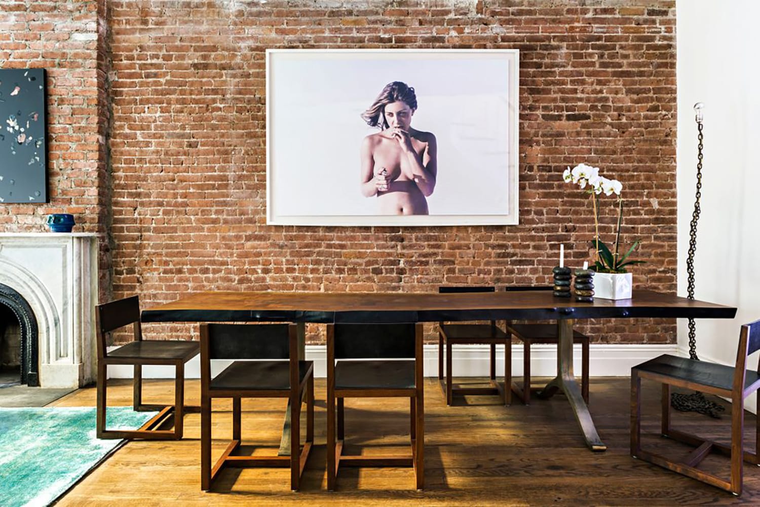 Modern dining room with brick wall, rectangular wooden table, black chairs, orchid centerpiece, and large framed artwork.