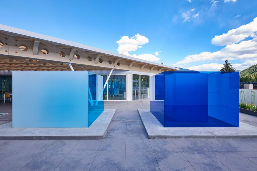 Outdoor art installation with two blue-toned glass structures under a clear sky and fluffy clouds.