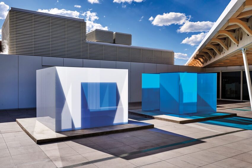 Modern architectural installation with large white and blue cubes on a sunny rooftop with a blue sky background.